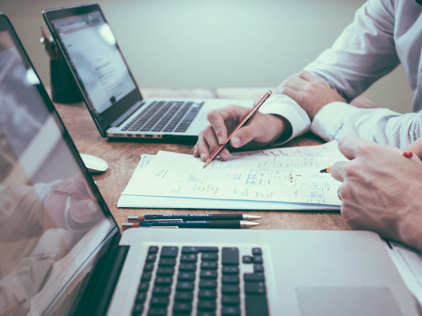 Two people comparing bid spreadsheets side by side at a desk with laptops